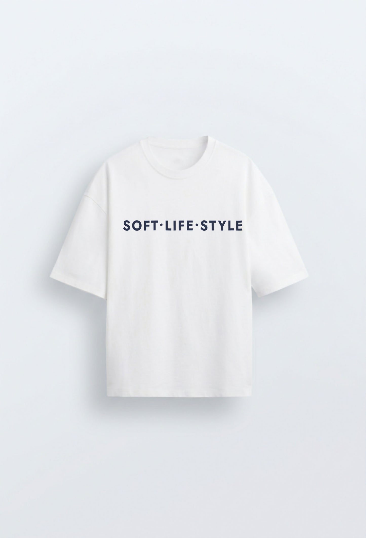 White oversized heavyweight tee with navy blue typographic print reading "SOFT·LIFE·STYLE" centred on the chest, on a clean light blue background.