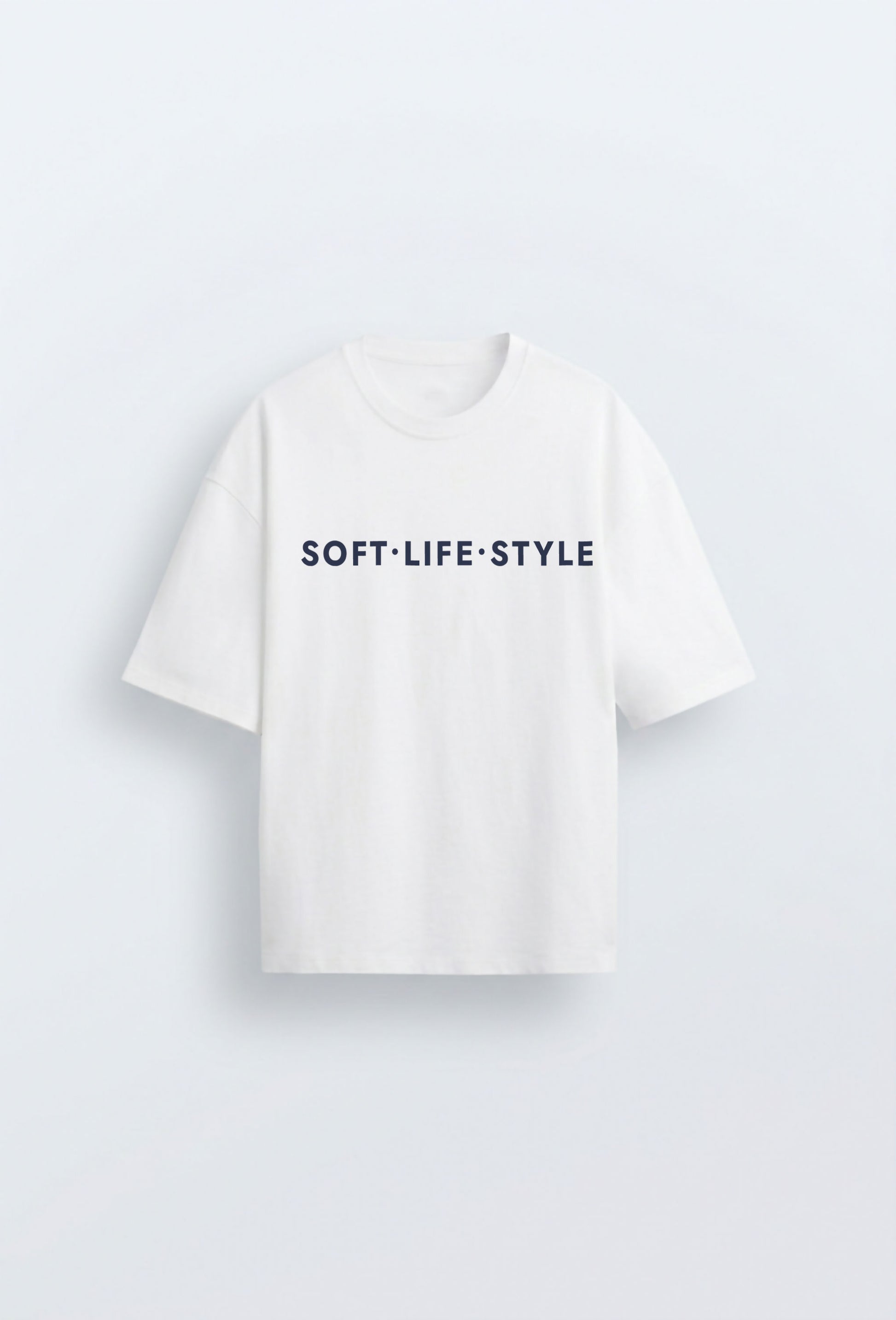 White oversized heavyweight tee with navy blue typographic print reading "SOFT·LIFE·STYLE" centred on the chest, on a clean light blue background.